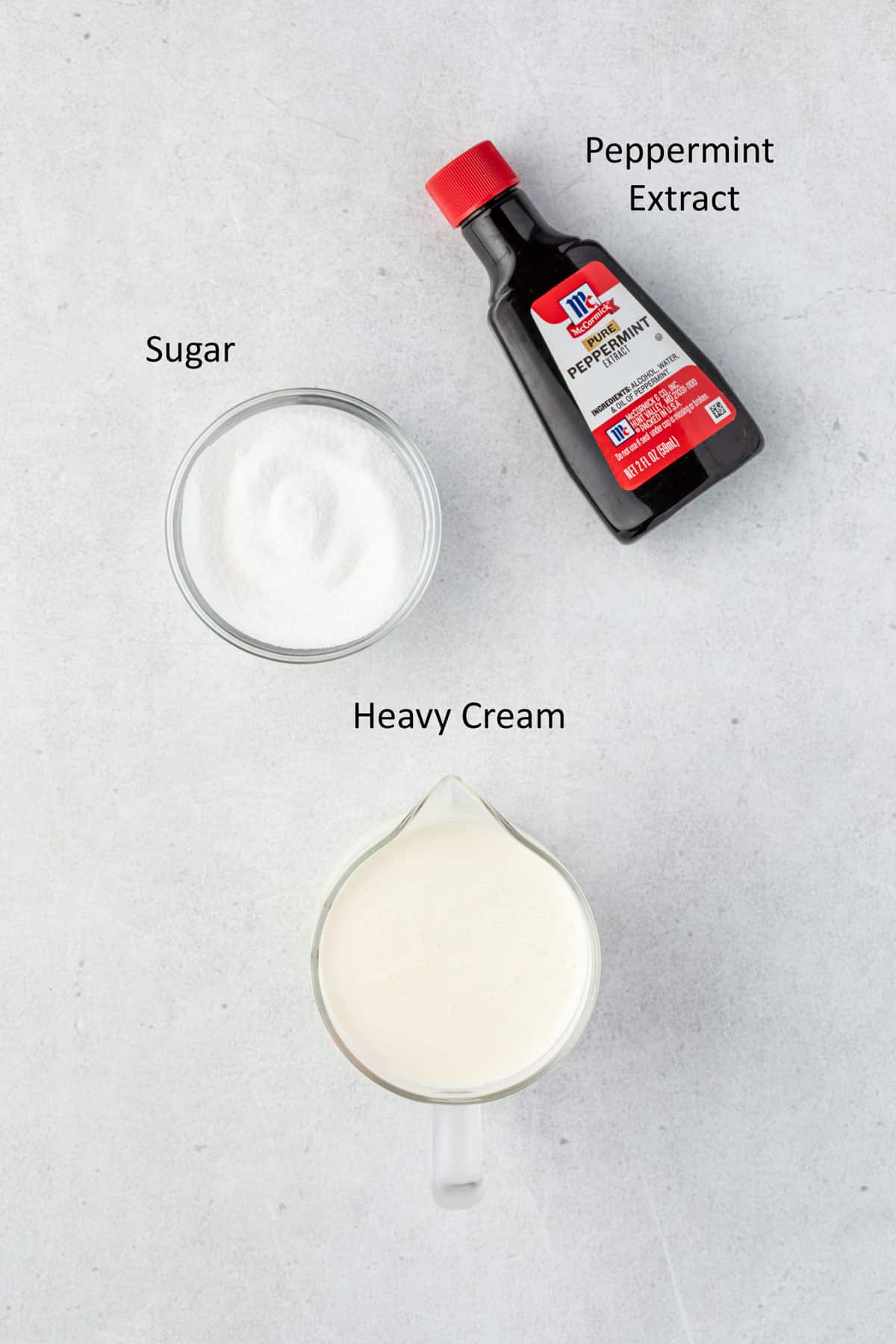 Whipping cream, bowl of sugar, and bottle of peppermint extract.