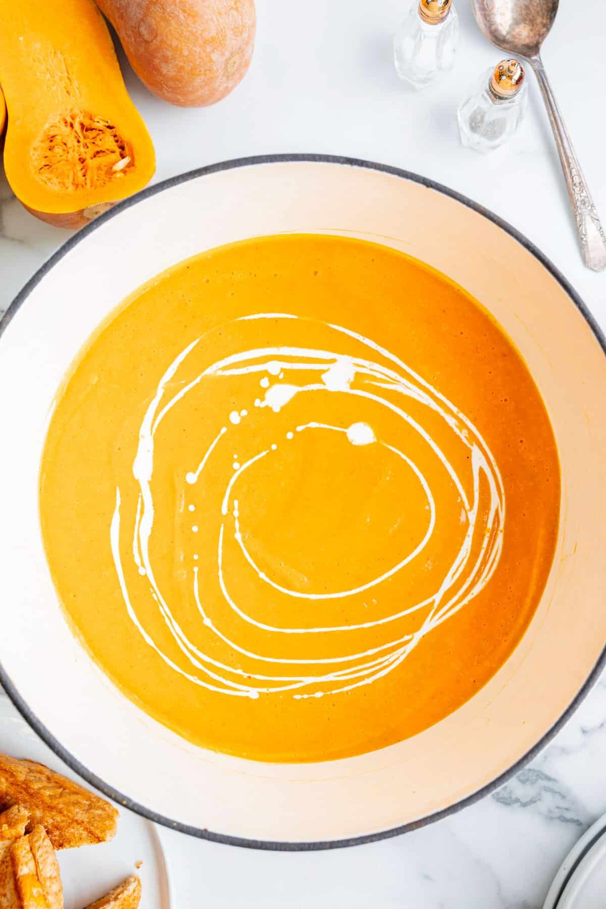 Orange butternut squash soup in a dutch oven with cream swirls in the soup.