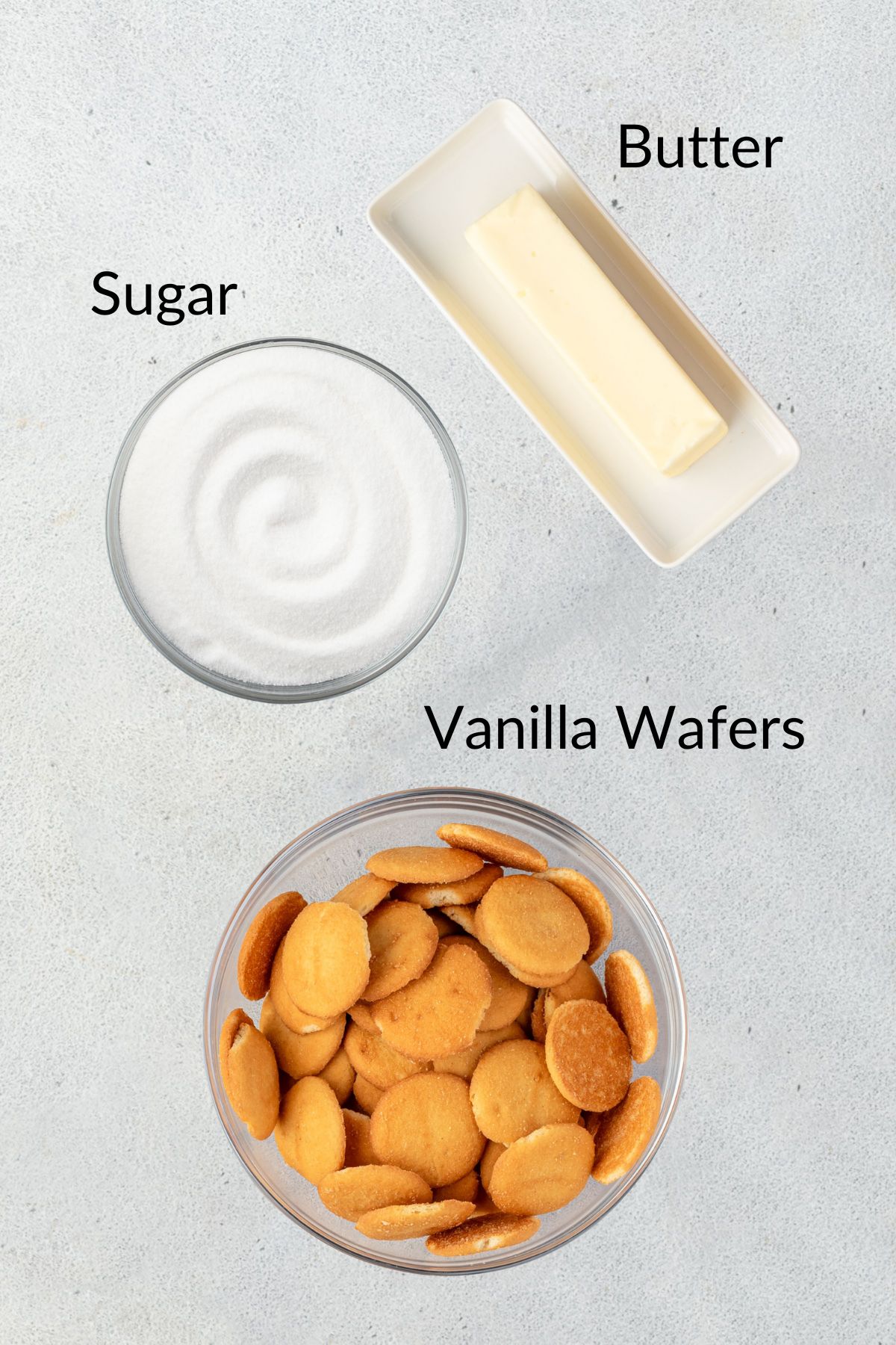 A stick of butter, bowl of sugar, and bowl of vanilla wafer cookies.