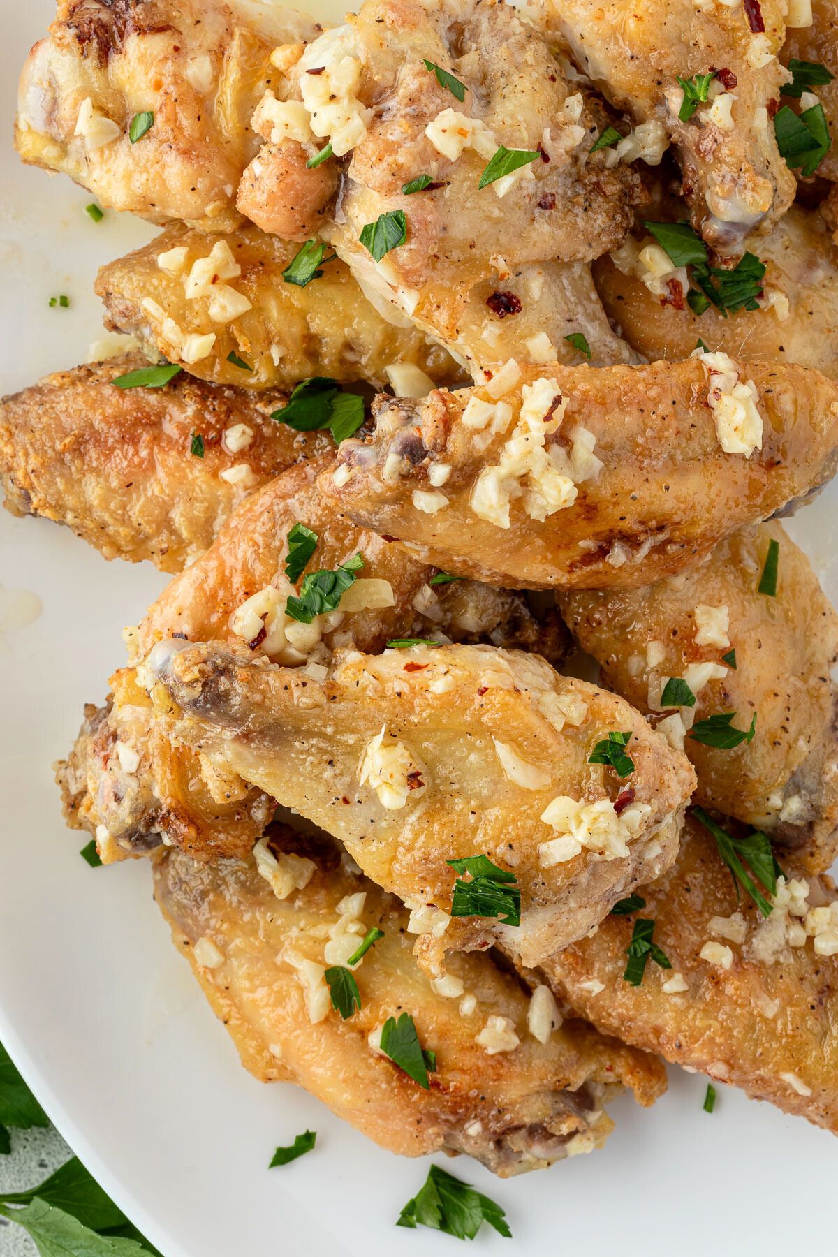 Platter of golden brown chicken wings topped with garlic butter.