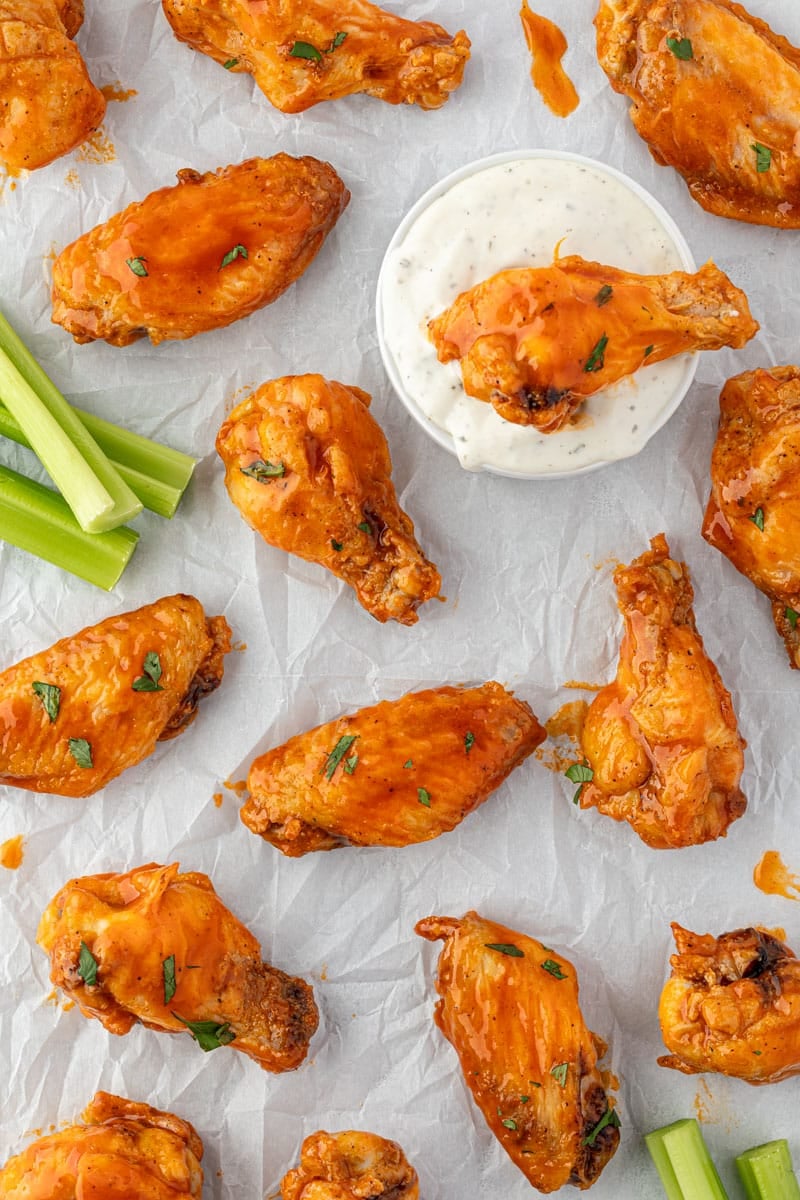 Wings spread out on parchment paper with space between each one and one dipped in a bowl of ranch.