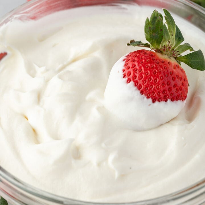 Dipped strawberry sitting in a bowl of whipped cream.