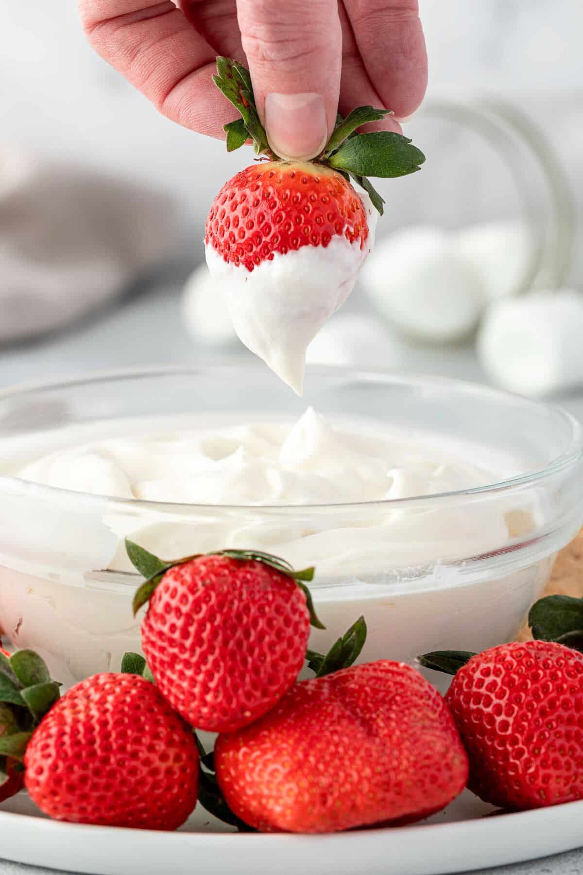 Strawberry dipped in marshmallow frosting held over a bowl of whipped forsting.