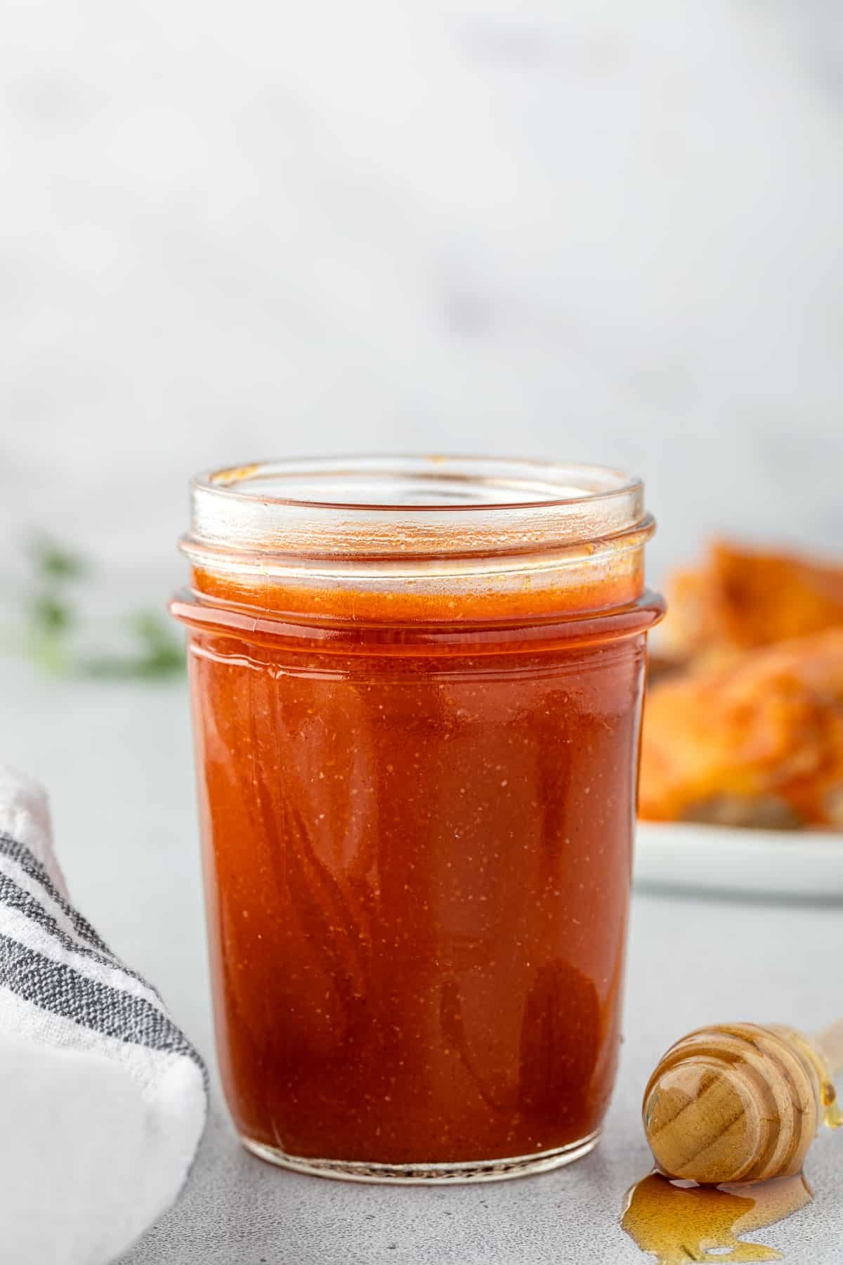 A jar of sauce with a honey dipper and a pool of honey next to it.