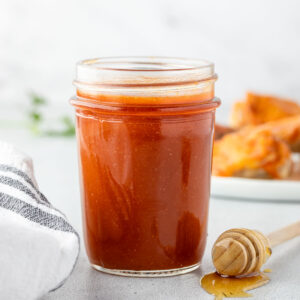 A jar of honey buffalo sauce with a honey dipper an a platter of wings.