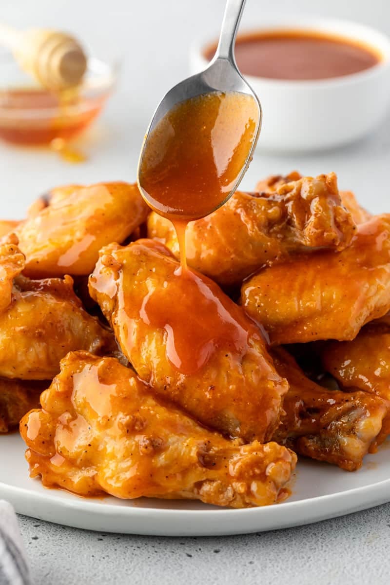A spoon dripping sauce onto a platter of wings. 