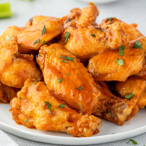 Saucy honey buffalo wings garnished with parsley on a round platter.