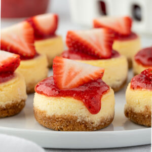Mini cheesecakes with strawberry sauce on a round plate.
