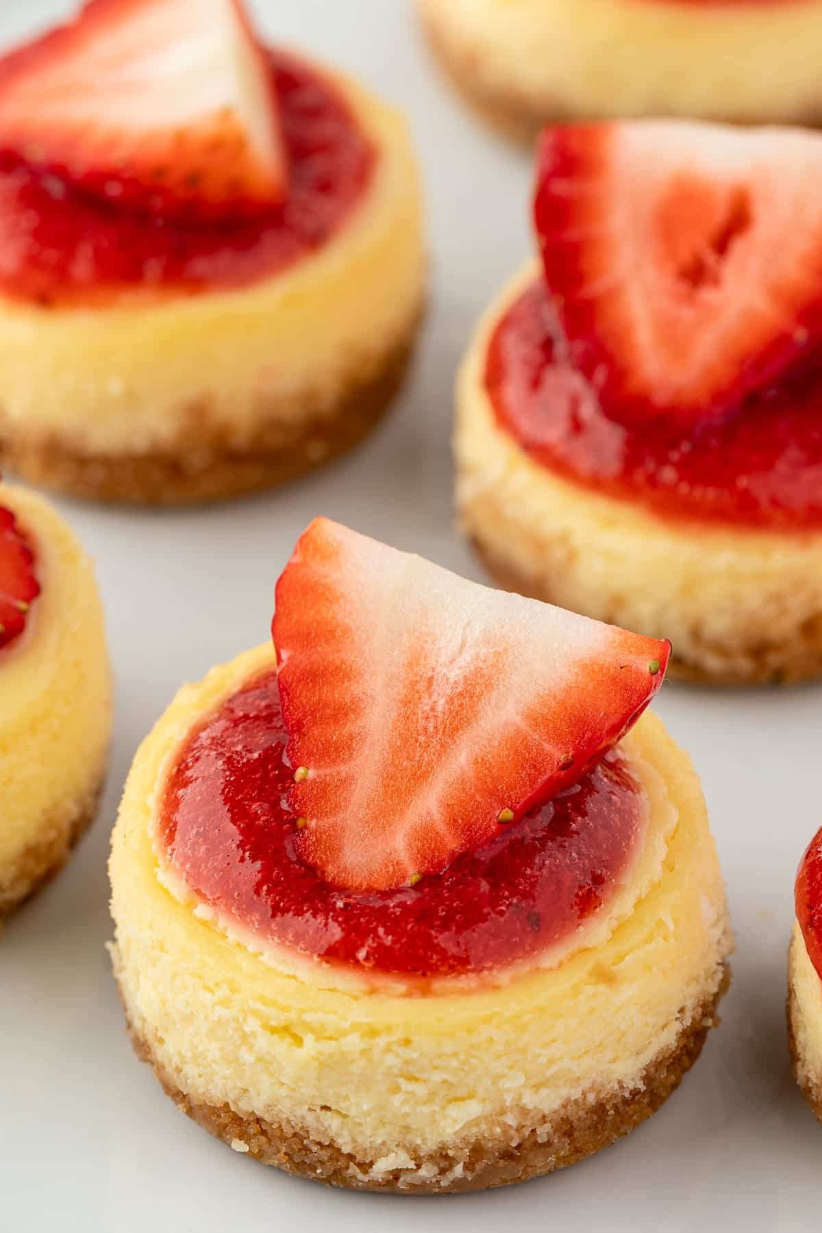 A platter of miniature strawberry cheesecakes topped with strawberry halves.