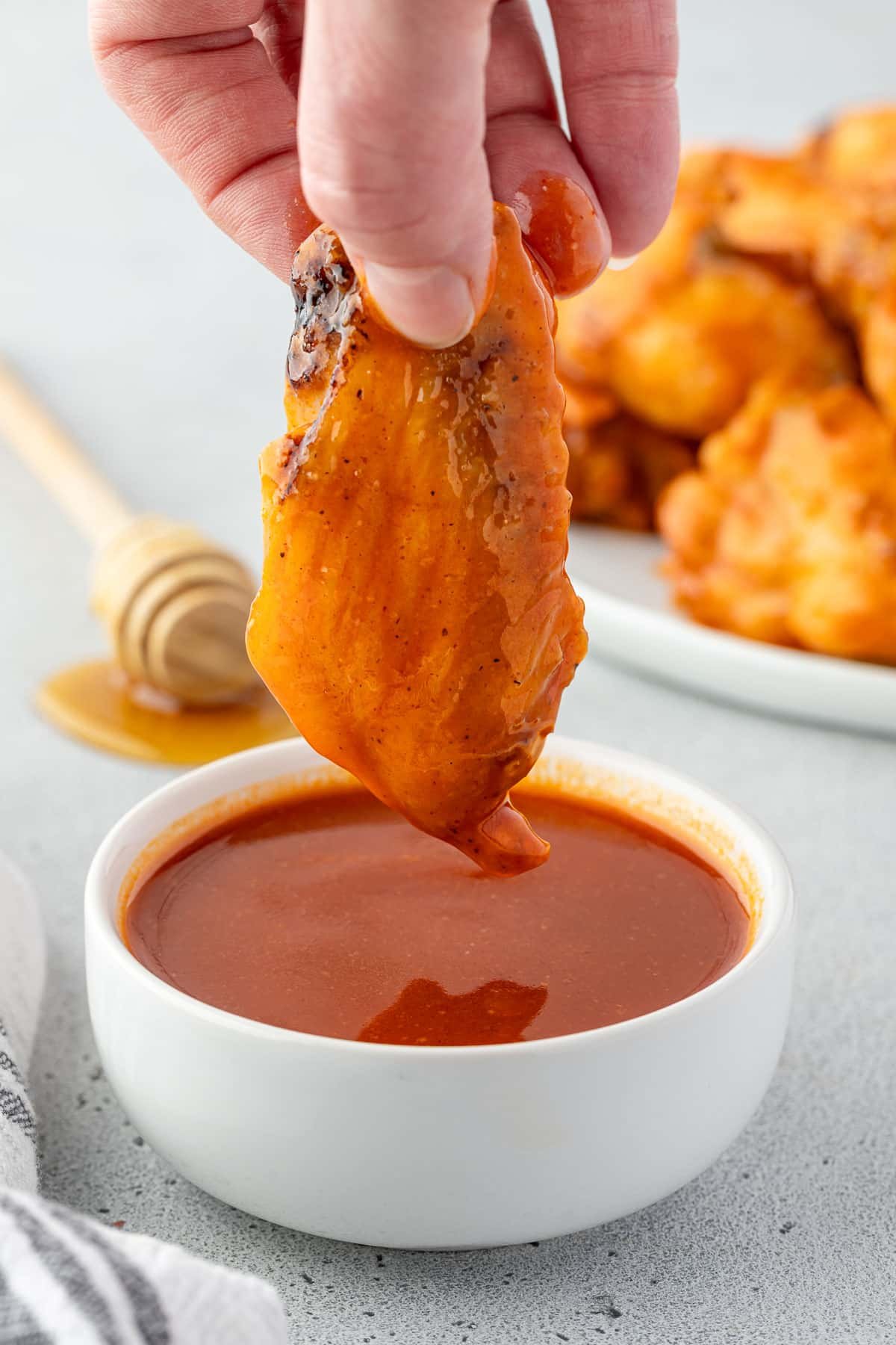 A hand holding a chicken wing and dipping it into a bowl of sauce.