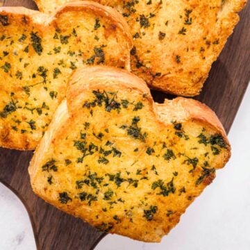 3 slices of texas toast garnished with chopped parsley on a wooden serving board.