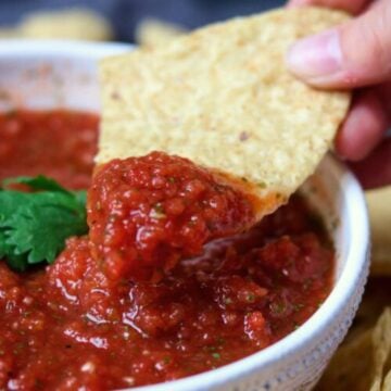 Tortilla chip with salsa on it held over a bowl of salsa.
