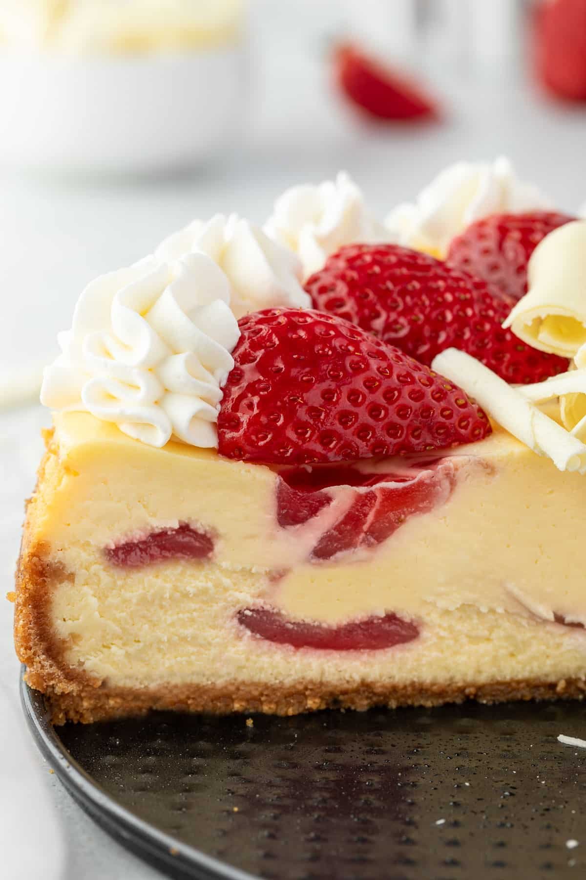The inside of a cut cheesecake topped with fresh strawberries and a dollops of whipped cream.