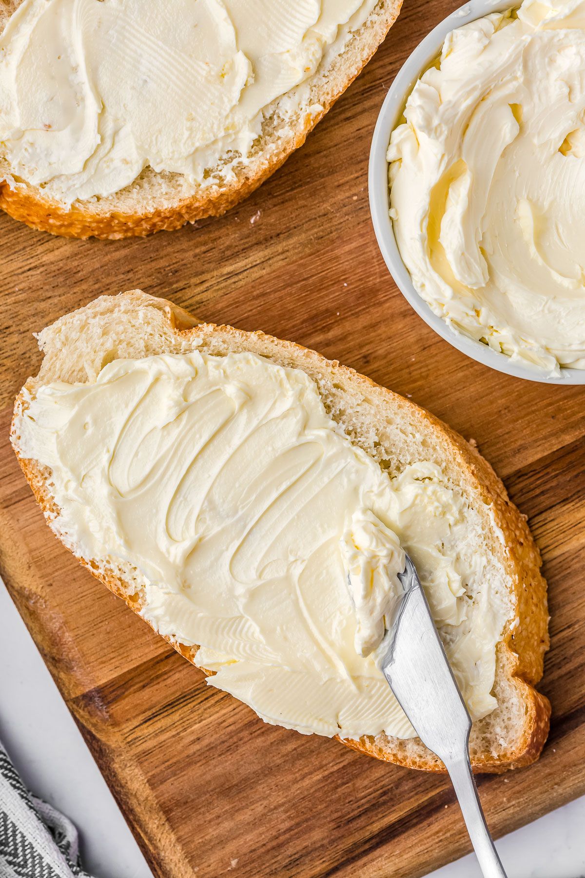 Spreading fresh butter on a slice of French bread with a butter knife.