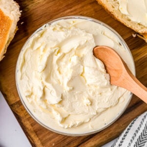 Fresh homamde butter in a bowl on a wooden board with bread slices around it.