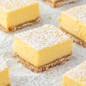 A lemon bar dusted with powdered sugar on parchment paper with several bars surrounding it.