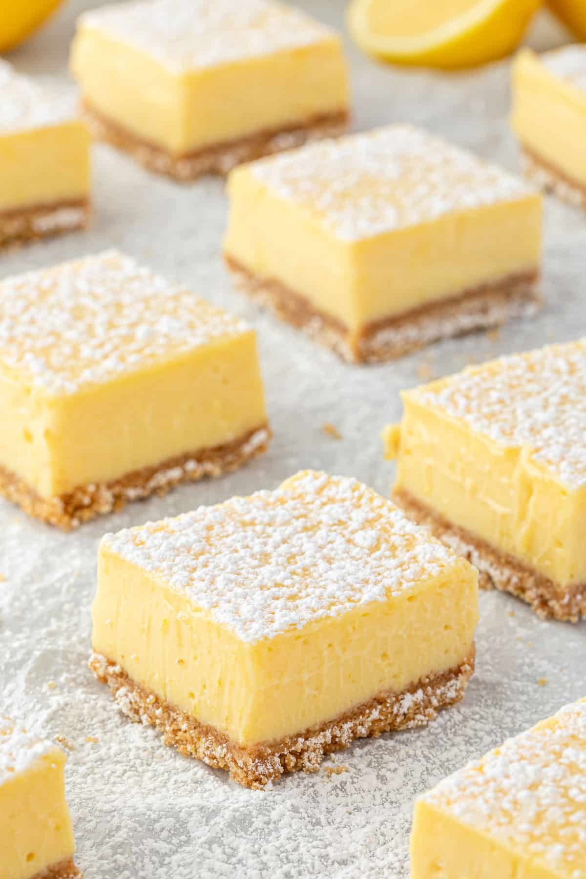 Creamy lemon bar squares with graham cracker crust on white parchment paper.