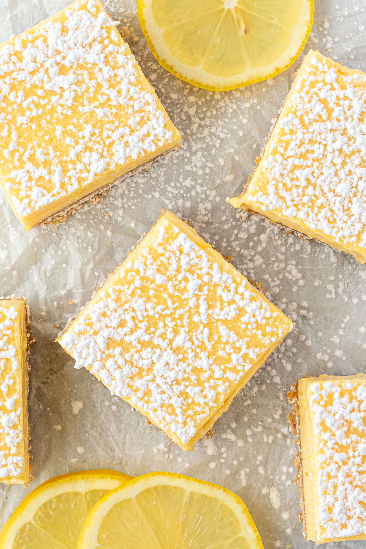 Lemon squares on white parchment dusted with powdered sugar, with 3 lemon slices.