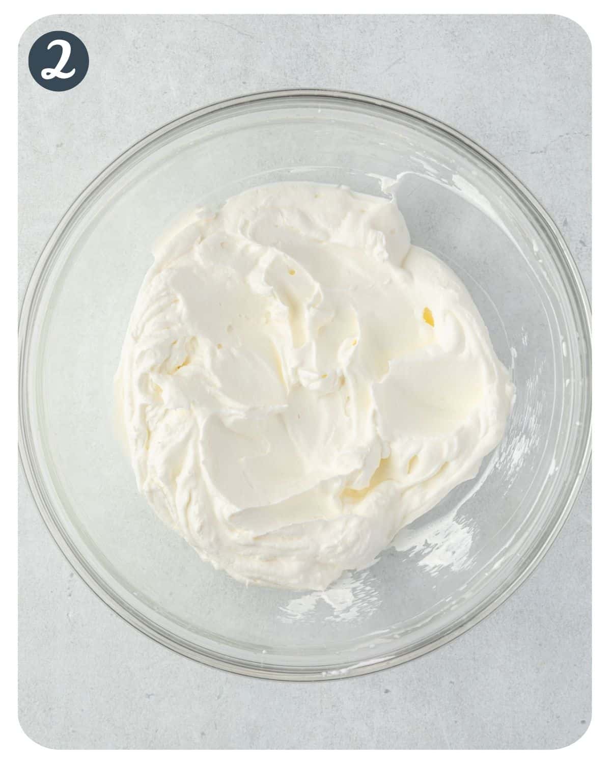 Whipped cream with stiff peaks in a glass bowl.