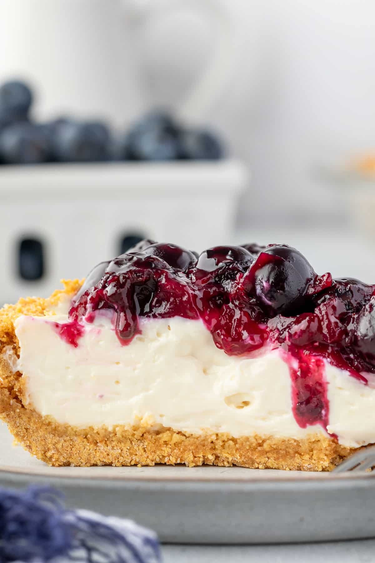 Slice of pie with graham cracker crust, creamy cheesecake filling, and blueberry pie filling.
