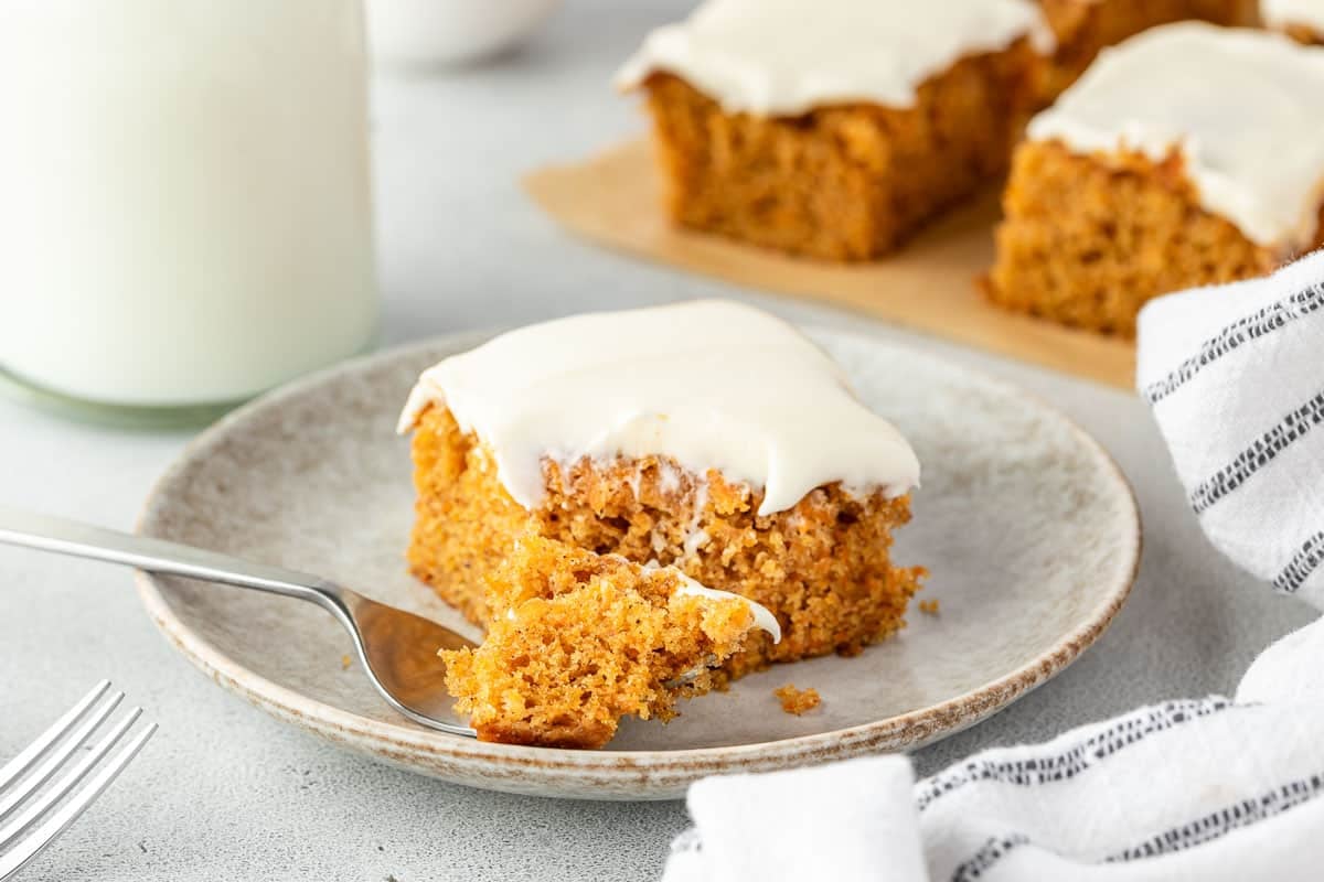 A slice of carrot cake with white frosting on a plate, with a fork taking a bite.