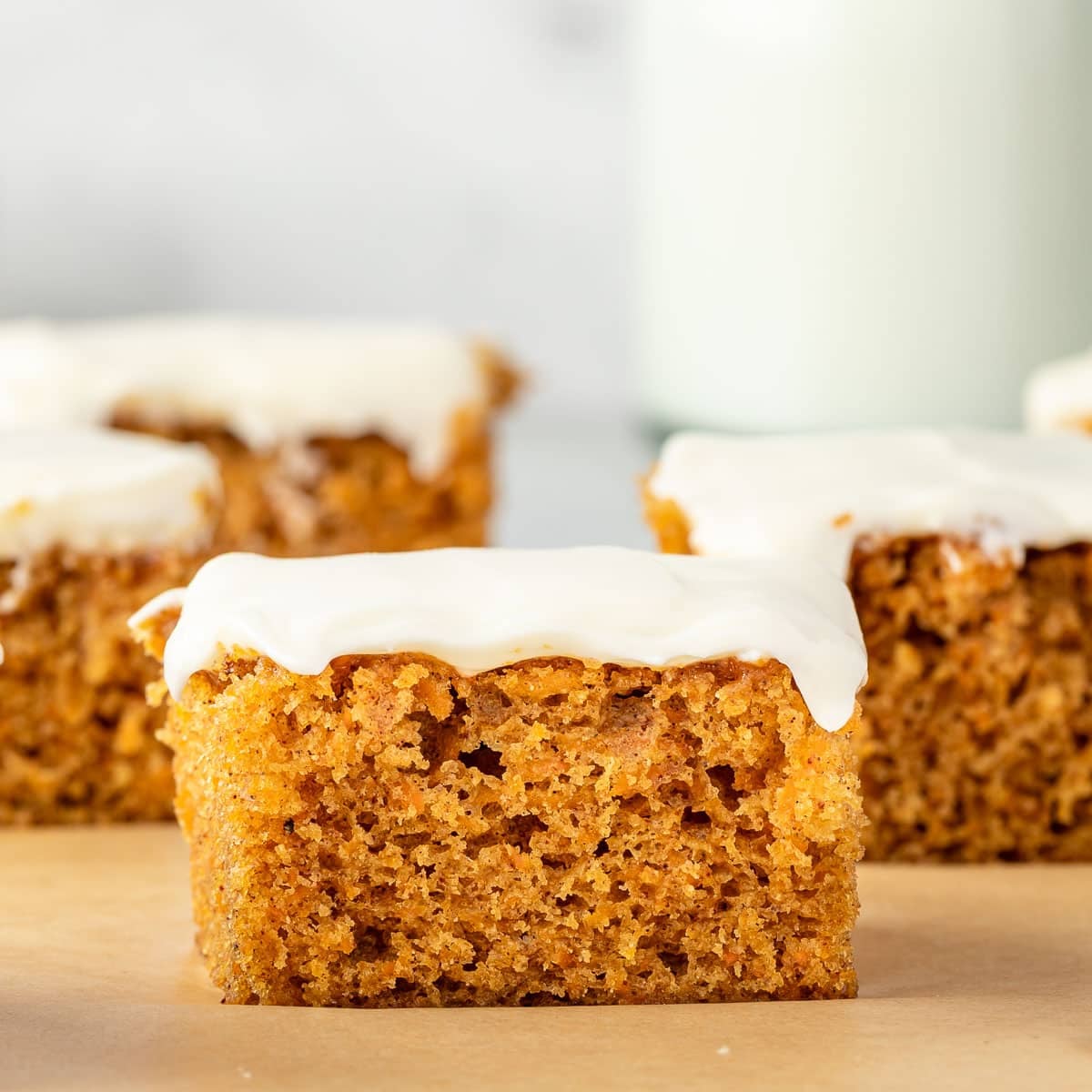 carrot cake squares topped with cream cheese frosting on brown parchment