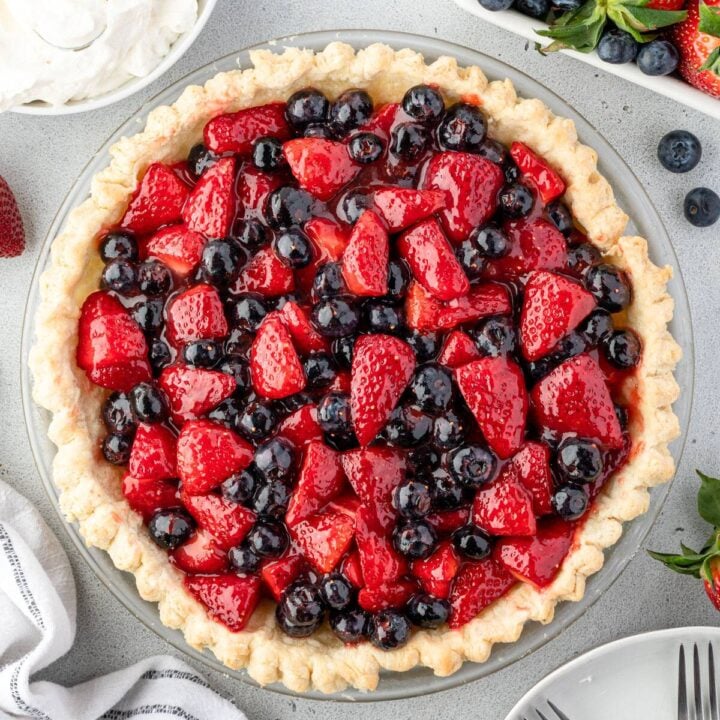 A freshly made fruit pie with a golden crust, filled with glossy red strawberries and fresh blueberries on a light grey surface.