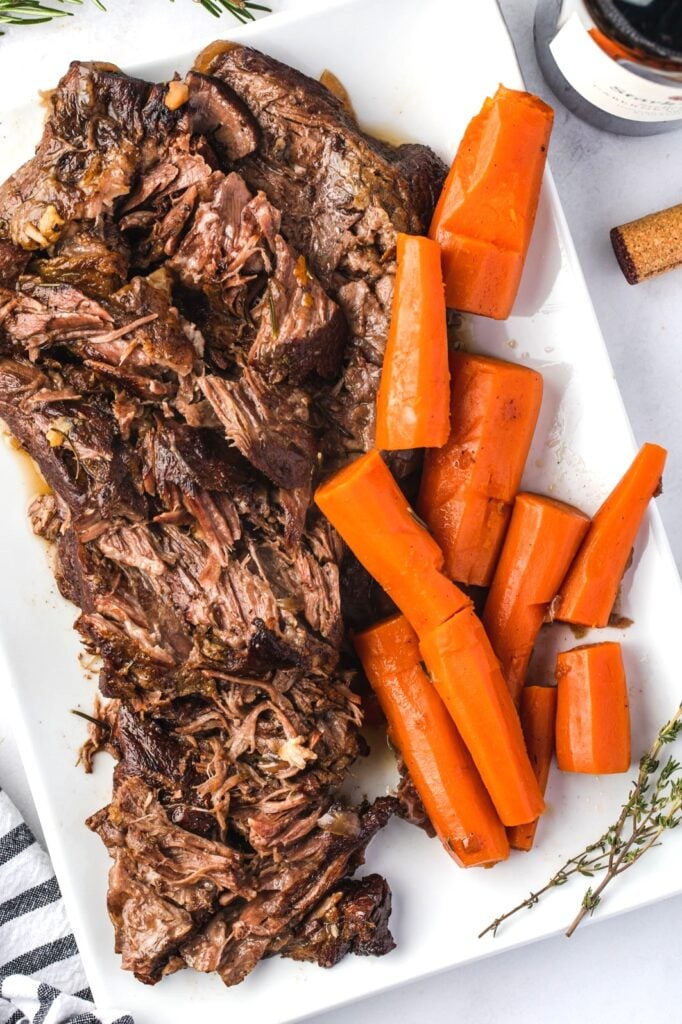 A white rectangular plate holds shredded pot roast and large pieces of cooked carrots. 