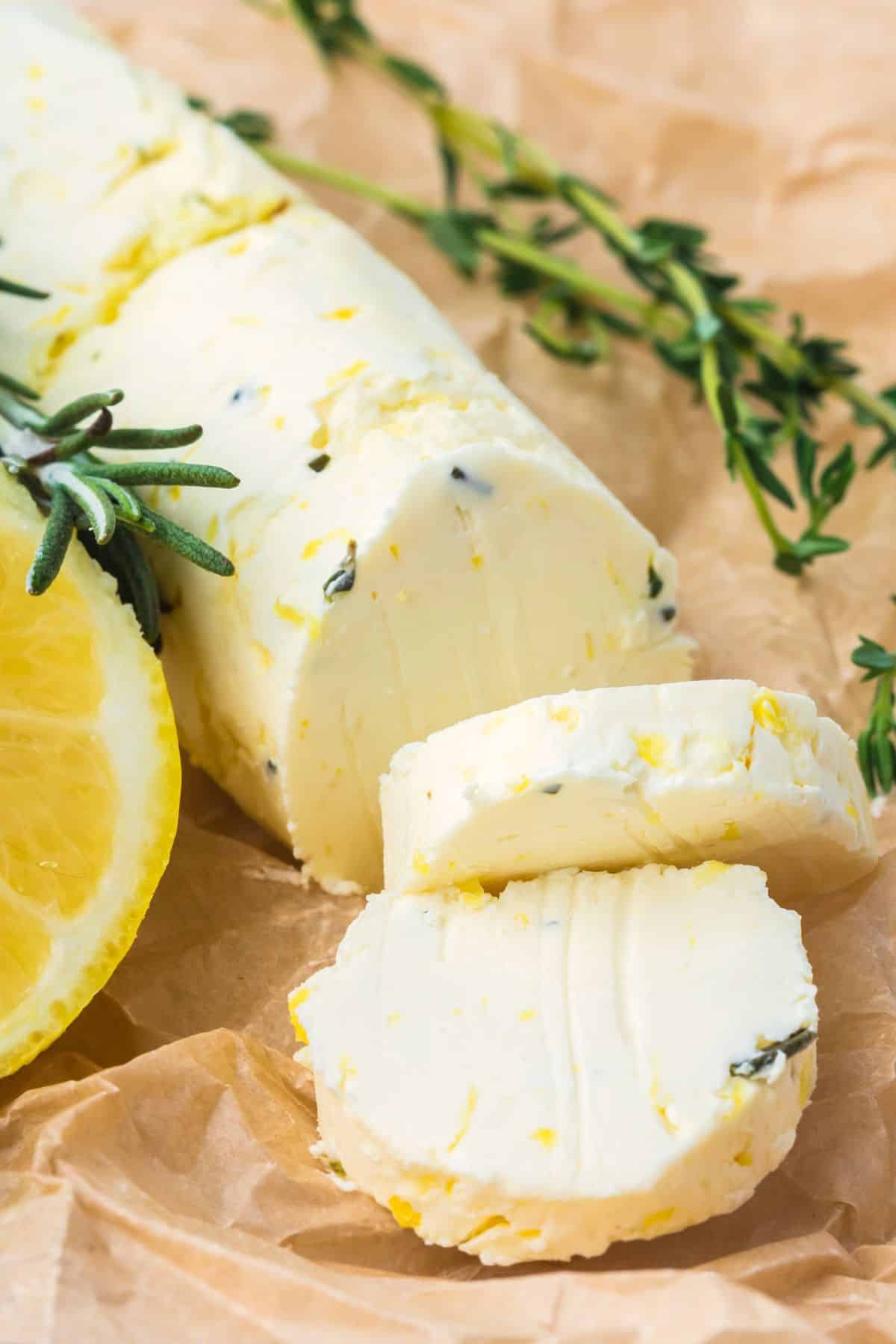 A cylindrical roll of herb-infused butter is sliced on parchment paper with leon and thyme around it.