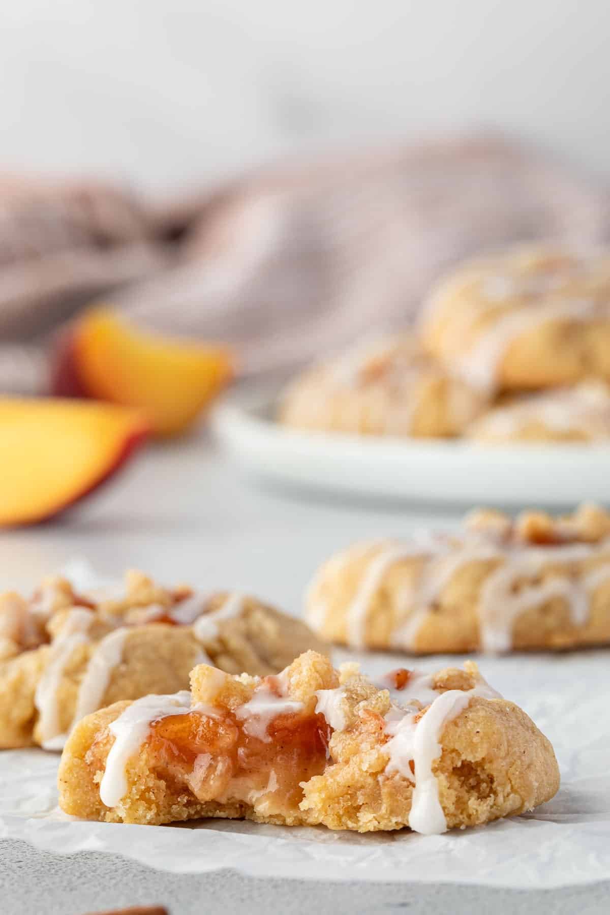 Freshly baked cookies filled with a peach filling and drizzled with white icing, cookie in front has a bite taken out.