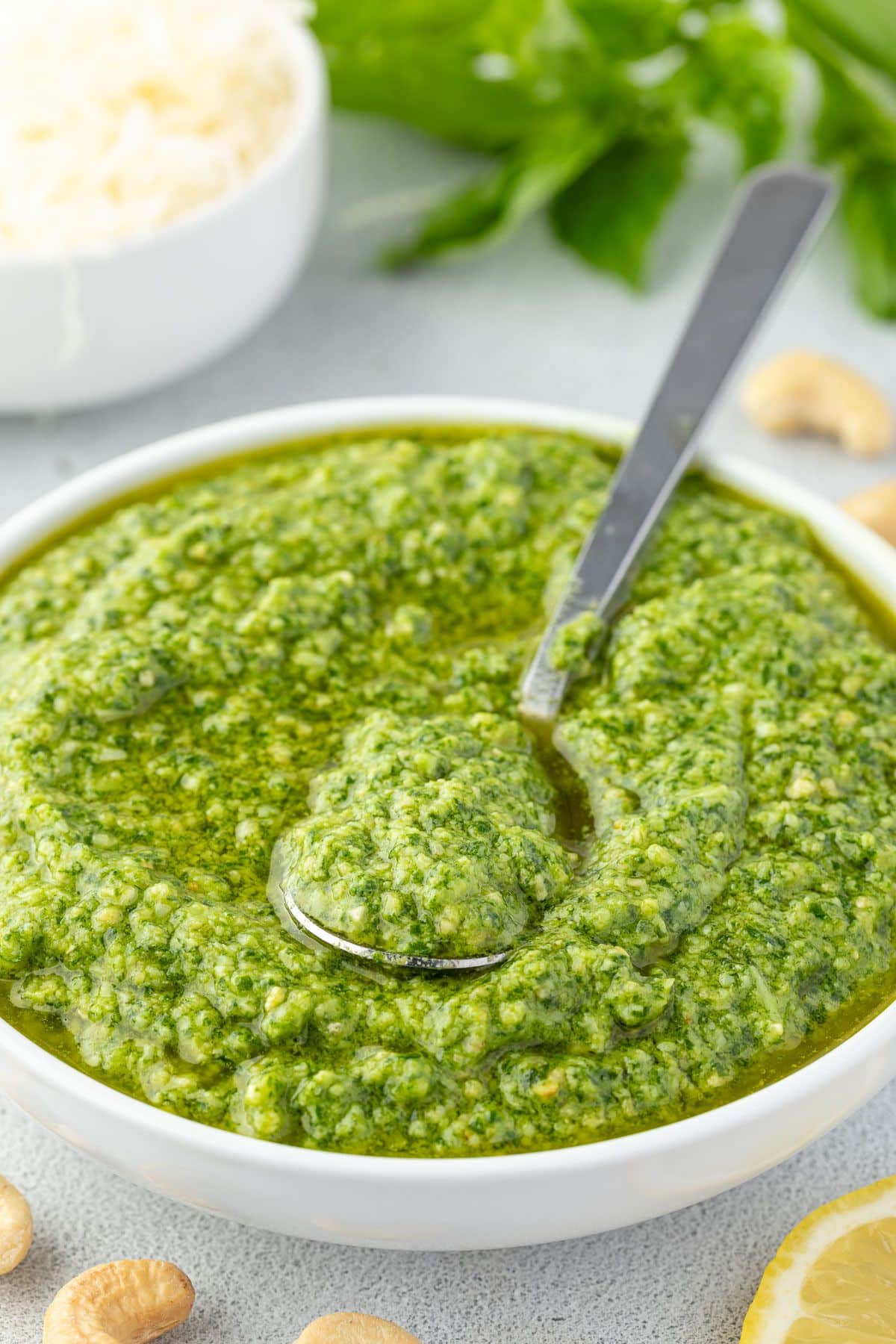 A white bowl of vibrant green pesto with a spoon scooping some of the sauce.