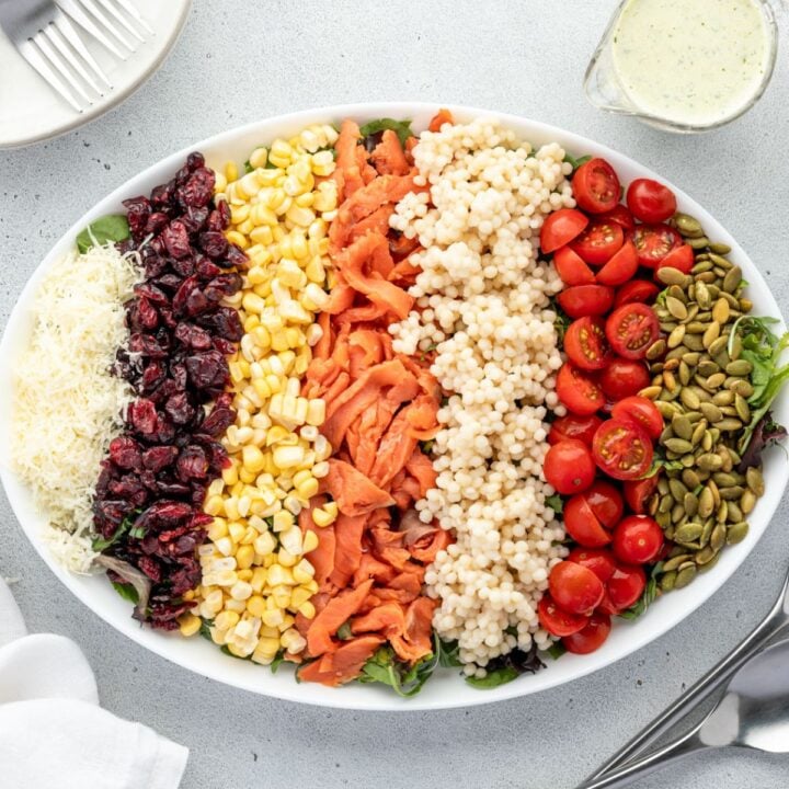 A white oval plate filled with a neatly arranged rainbow salad ingredients in rows.