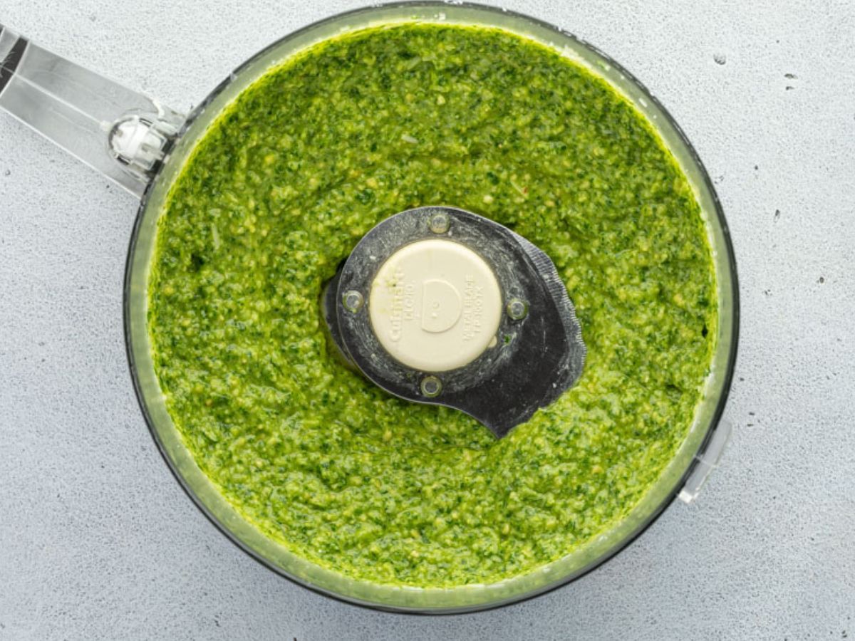 A food processor filled with freshly made green pesto sits on a light grey countertop.