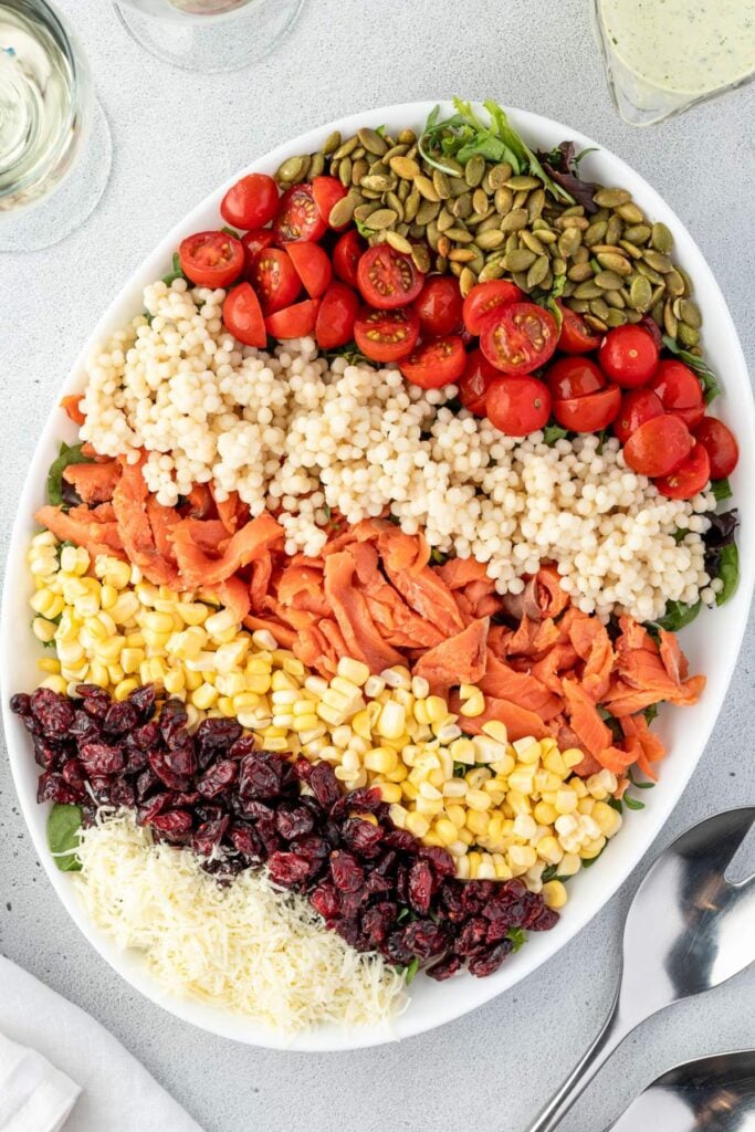 A large, white, oval platter is filled with rows of fresh ingredients for a salad.