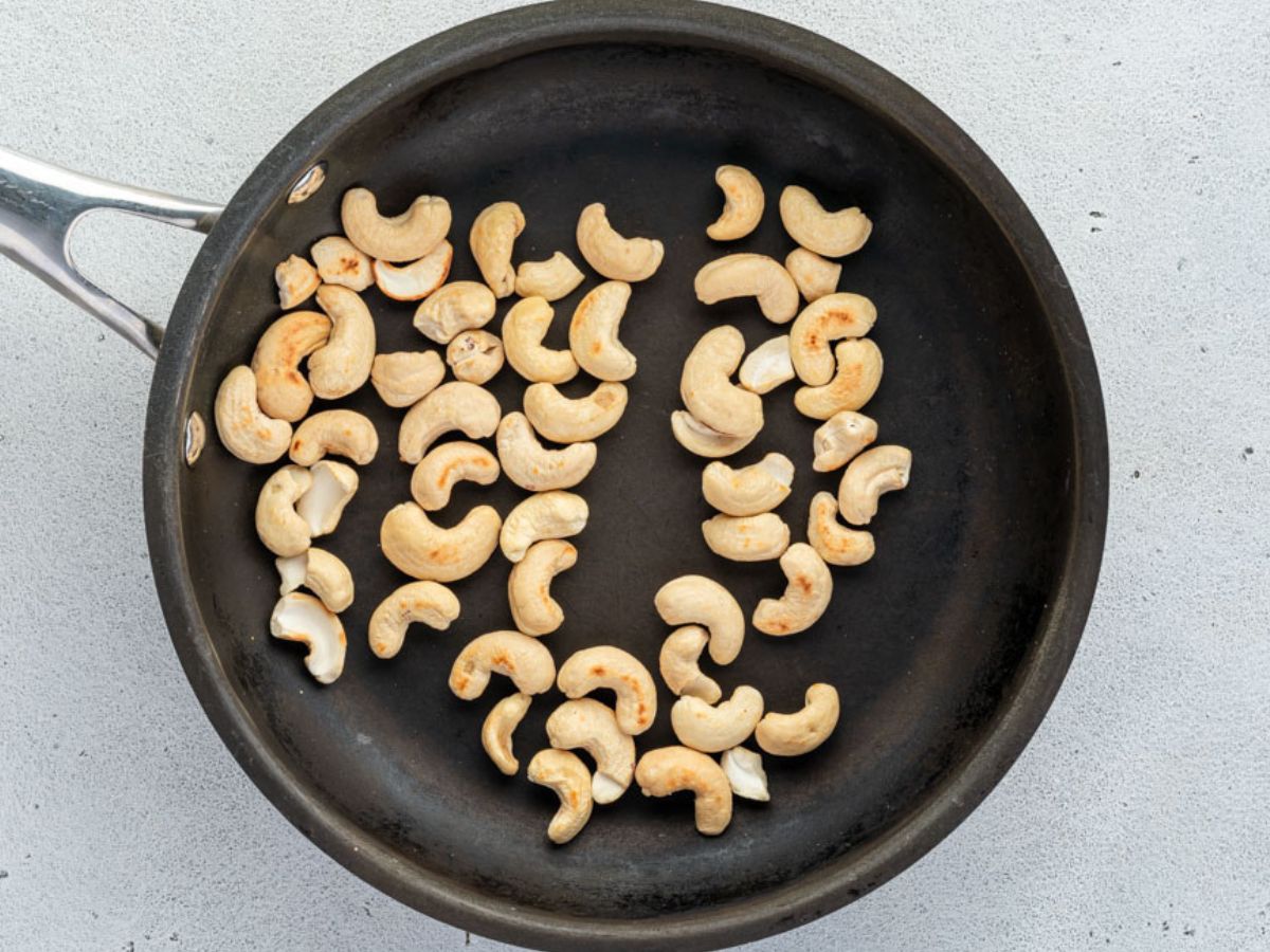 A black frying pan on a grey surface filled with cashew nuts.