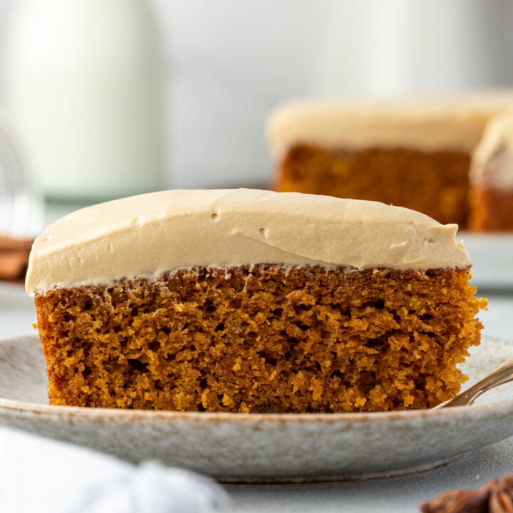 A slice of spiced pumpkin cake with a thick layer of cream cheese frosting on a ceramic plate, showcasing the simplicity of a one bowl cake.