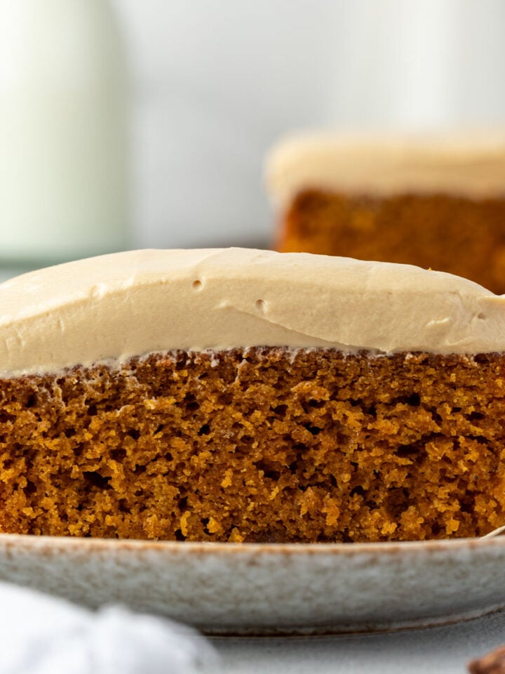 A slice of spiced pumpkin cake with a thick layer of cream cheese frosting on a ceramic plate, showcasing the simplicity of a one bowl cake.