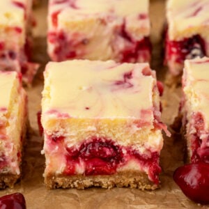 Cranberry cheesecake bars with a graham cracker crust on parchment paper.