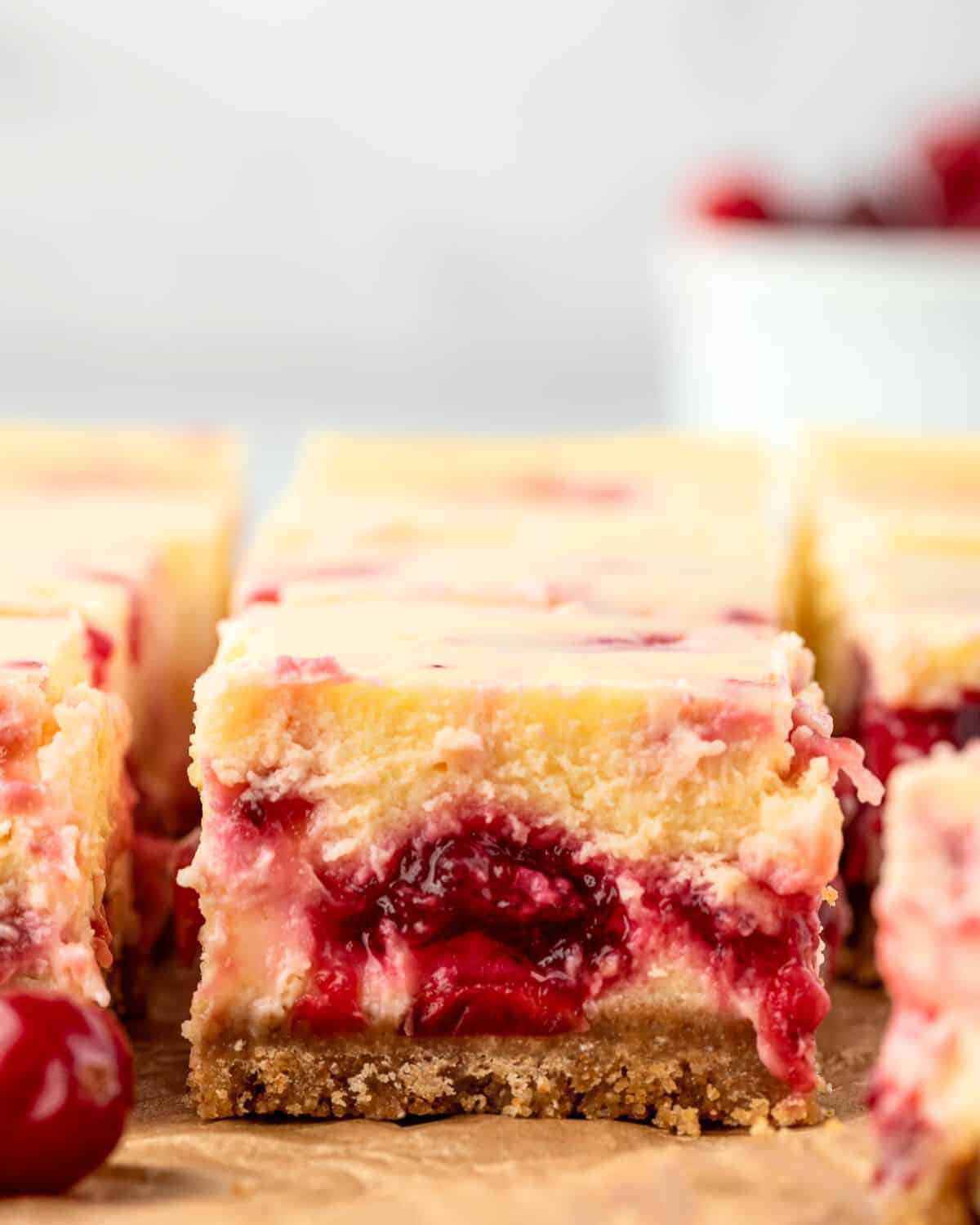 Individual squares of cranberry cheesecake bars with a creamy top layer and juicy cranberry filling in the center.