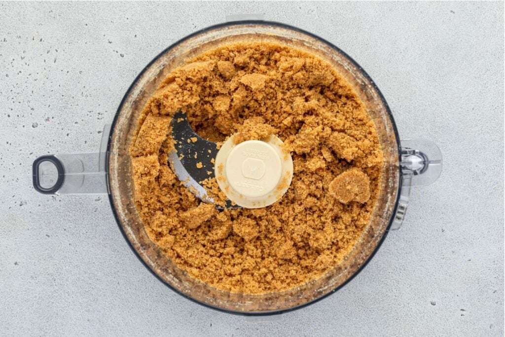 A food processor filled with crushed crumb mixture that looks like sand.