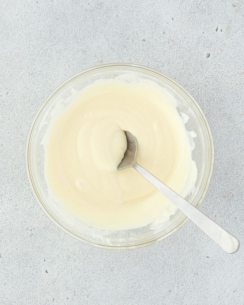 A glass bowl containing a creamy white cheesecake mixture with a spoon resting inside.