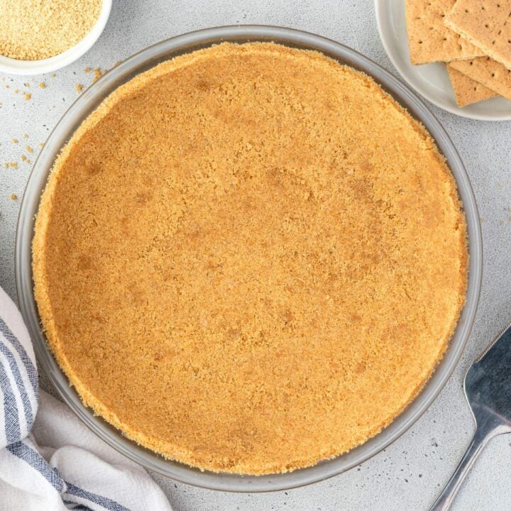 A no-bake graham cracker pie crust in a glass dish rests on a gray surface.