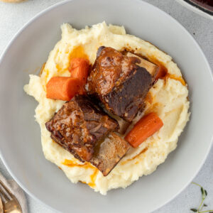 A plate of mashed potatoes topped with beer-braised short ribs and carrots.