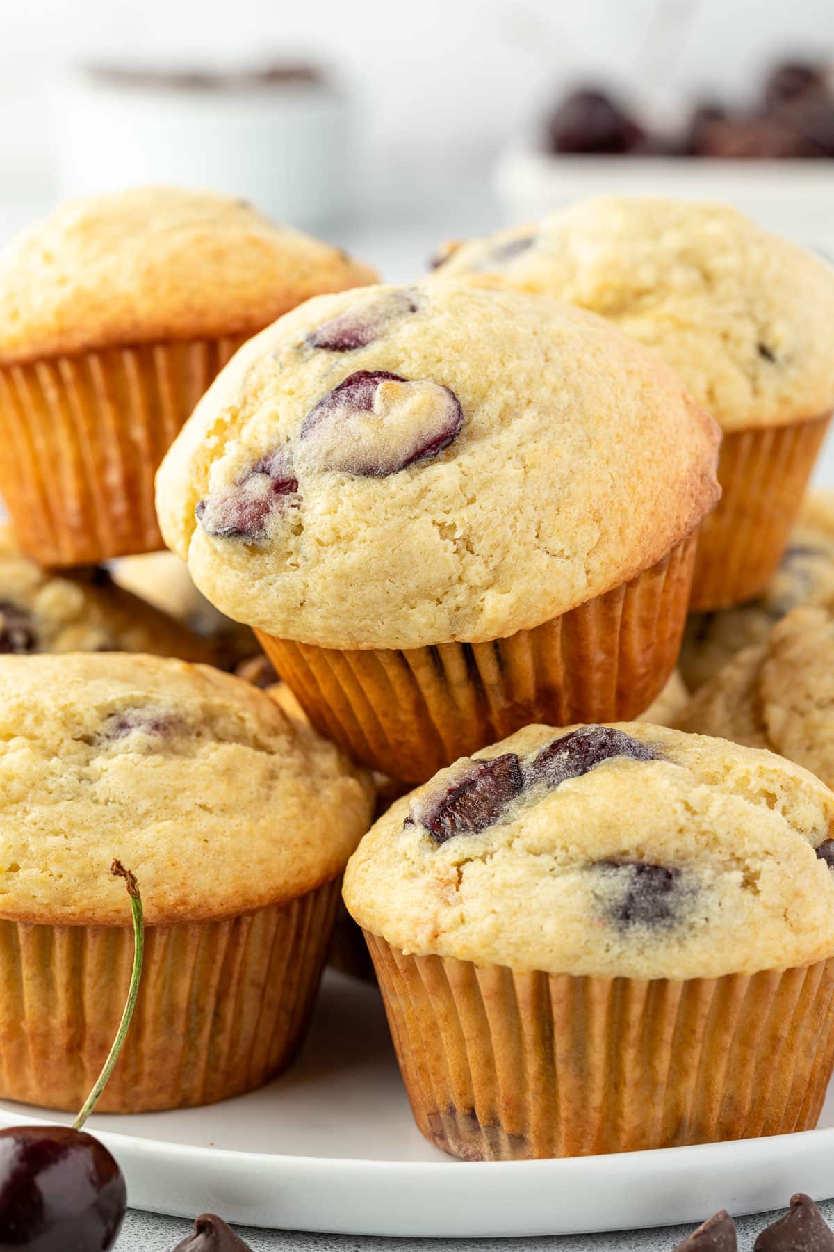 A pile of chocolate cherry muffins with visible pieces of dark fruit and chocolate chips on a white plate.