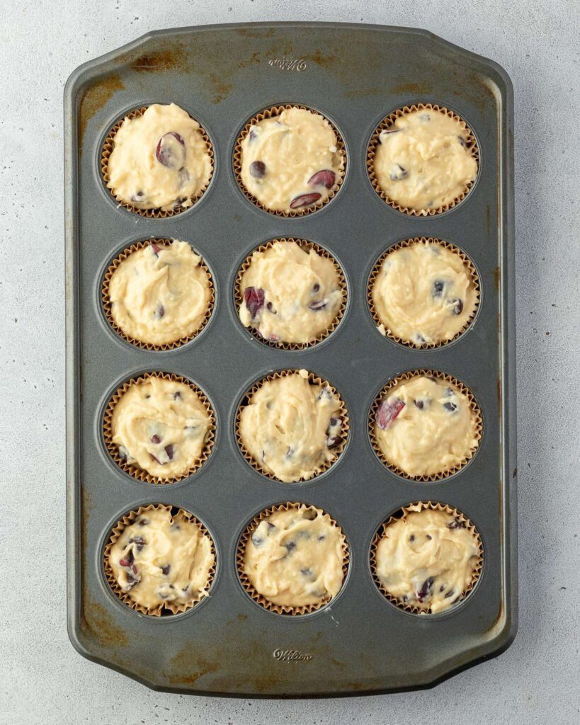 A muffin tray filled with uncooked batter, each lined with paper cups.