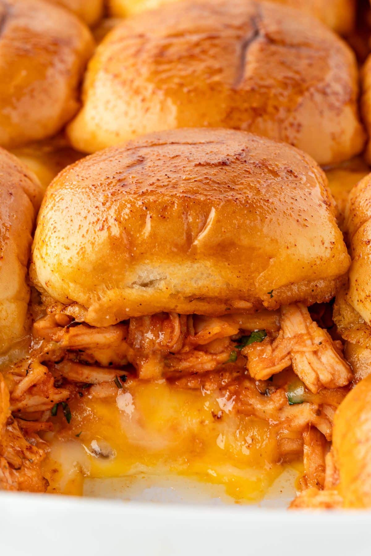 Close-up of cheesy BBQ chicken sliders with a golden brown top and melted cheese oozing out.