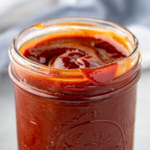 Open glass jar filled with thick, reddish-brown barbecue sauce, with sauce on the rim.