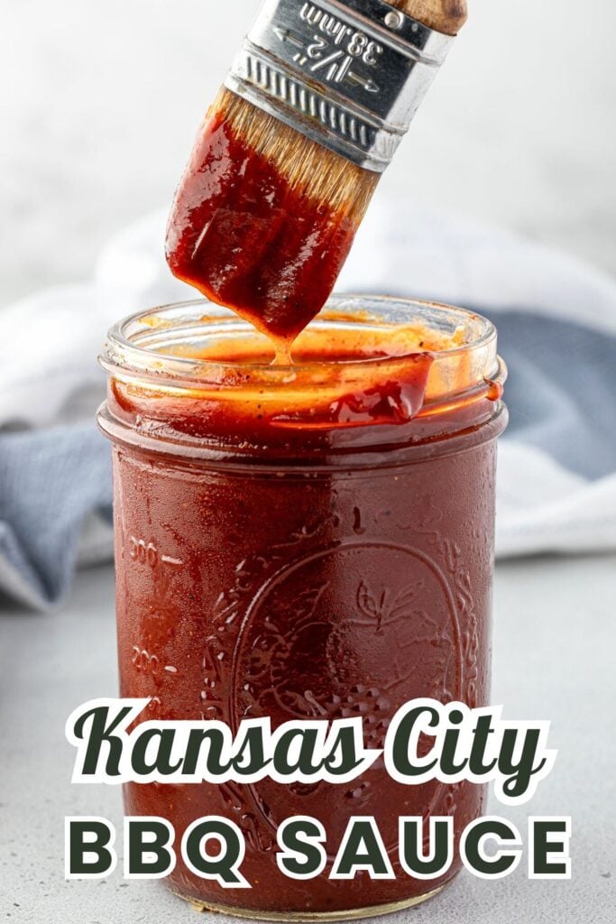 A brush covered in BBQ sauce rests on a jar filled with thick, dark red Kansas City BBQ sauce.