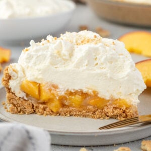 A slice of peach cream pie with a graham cracker crust and whipped cream on a plate.