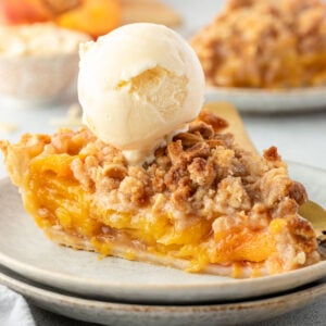A slice of peach crumble pie topped with a scoop of vanilla ice cream on a plate.